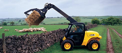 A telehandler lifting hay bales on a farm